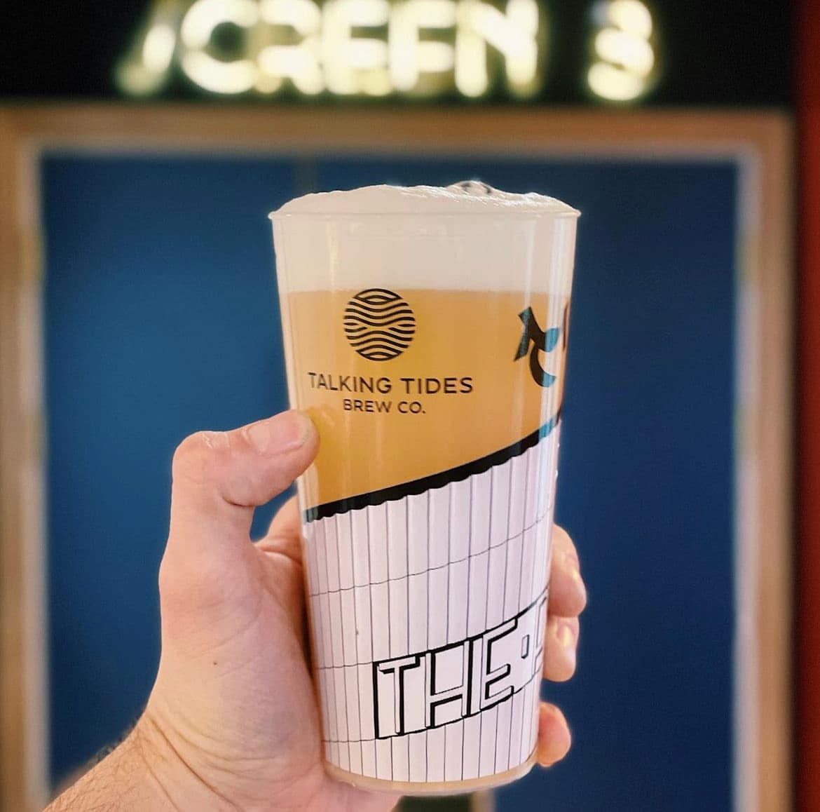 A printed reusable pint cup held up at a bar